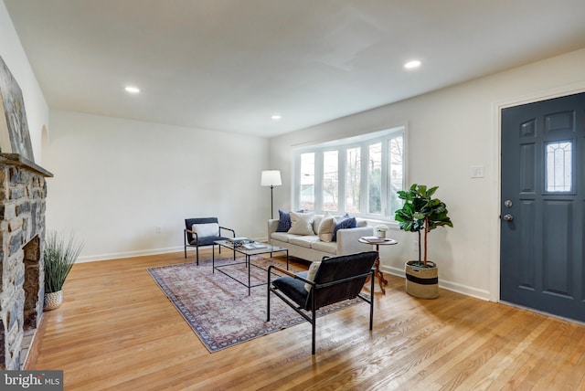 living area with a stone fireplace, light wood-style flooring, recessed lighting, and baseboards