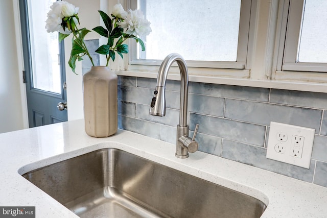 room details featuring a sink, light stone countertops, and tasteful backsplash