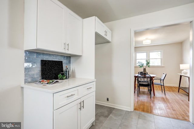 kitchen with tasteful backsplash, white cabinetry, light countertops, and baseboards