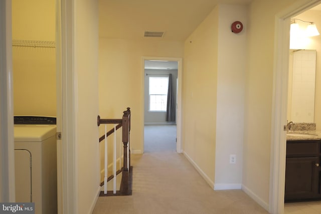 corridor featuring visible vents, an upstairs landing, light carpet, washer / dryer, and a sink