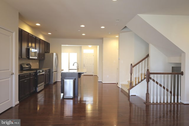 kitchen with light stone counters, dark wood finished floors, an island with sink, recessed lighting, and appliances with stainless steel finishes