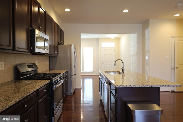 kitchen featuring dark wood-style floors, an island with sink, a sink, decorative backsplash, and stainless steel appliances