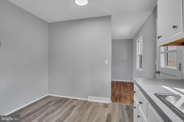 kitchen with visible vents, baseboards, light wood-style floors, white cabinets, and a sink