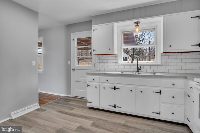 kitchen with baseboards, visible vents, a sink, decorative backsplash, and light wood-type flooring