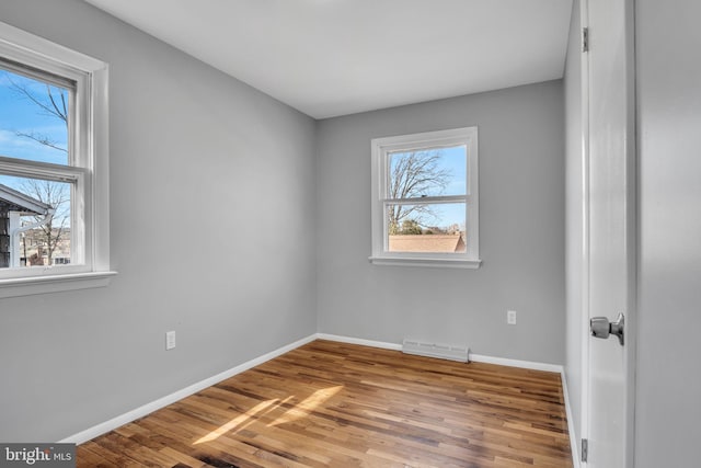 empty room featuring wood finished floors, visible vents, a wealth of natural light, and baseboards