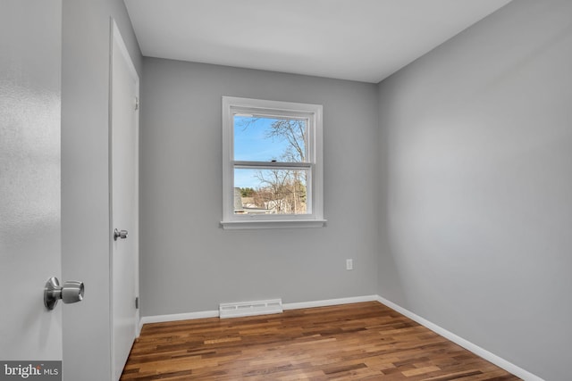 empty room featuring wood finished floors, visible vents, and baseboards