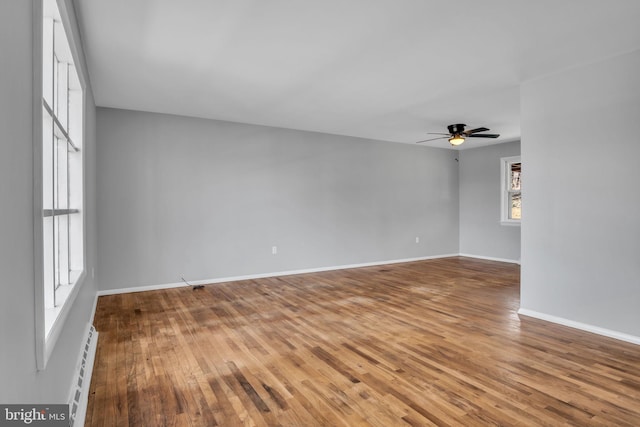 empty room with hardwood / wood-style floors, a ceiling fan, baseboards, and a baseboard heating unit