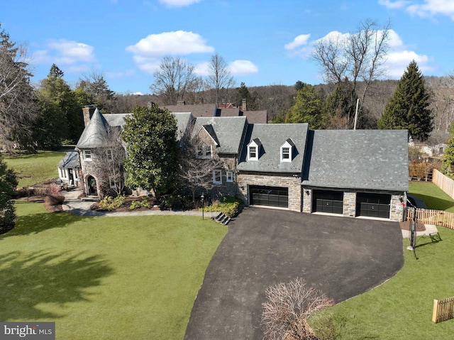 view of front facade featuring a front lawn, fence, stone siding, and aphalt driveway