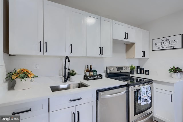 kitchen featuring appliances with stainless steel finishes, white cabinetry, light countertops, and a sink