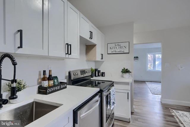 kitchen featuring baseboards, light wood-style flooring, a sink, white cabinets, and appliances with stainless steel finishes