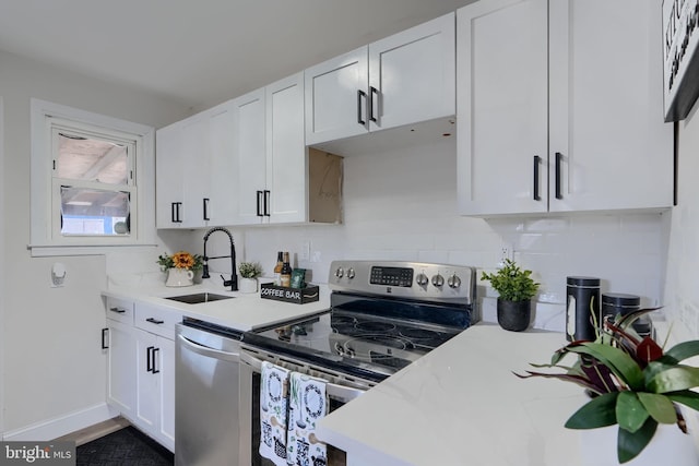 kitchen with baseboards, decorative backsplash, appliances with stainless steel finishes, white cabinetry, and a sink