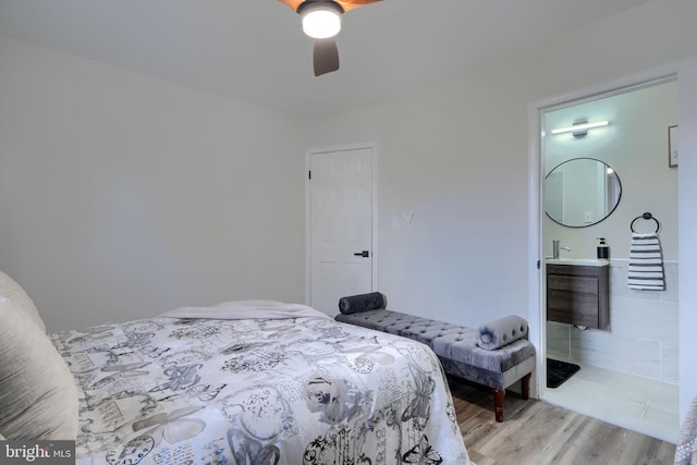 bedroom featuring light wood finished floors, ensuite bathroom, and a ceiling fan