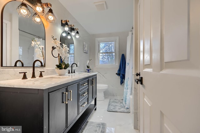 bathroom with tile walls, toilet, double vanity, and a sink