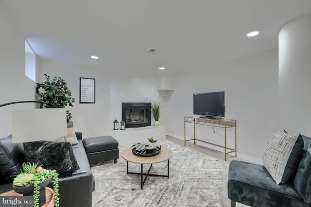 living room featuring a glass covered fireplace, recessed lighting, visible vents, and wood finished floors