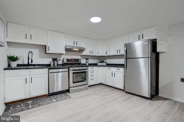 kitchen with under cabinet range hood, stainless steel appliances, dark countertops, and a sink