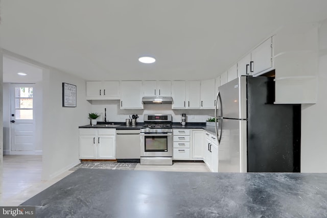 kitchen featuring white cabinetry, dark countertops, under cabinet range hood, and stainless steel appliances