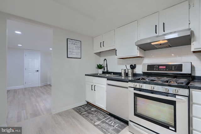 kitchen with dark countertops, under cabinet range hood, decorative backsplash, stainless steel gas range, and a sink