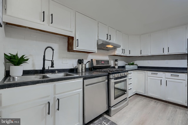 kitchen with a sink, under cabinet range hood, appliances with stainless steel finishes, white cabinetry, and backsplash