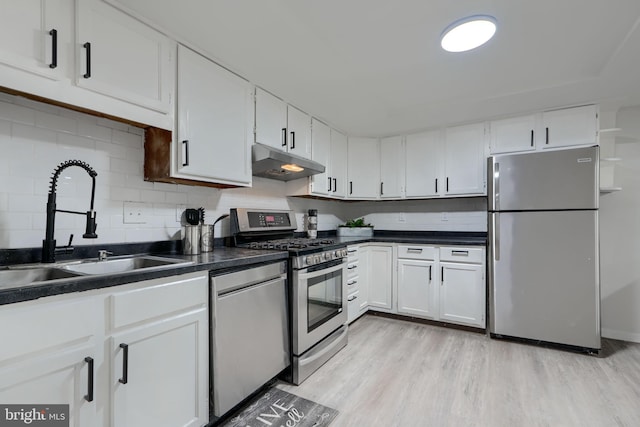 kitchen featuring under cabinet range hood, appliances with stainless steel finishes, dark countertops, and a sink