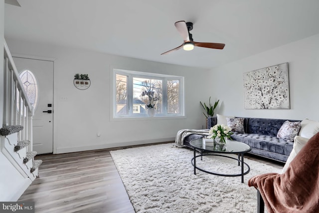 living area featuring stairs, wood finished floors, baseboards, and ceiling fan