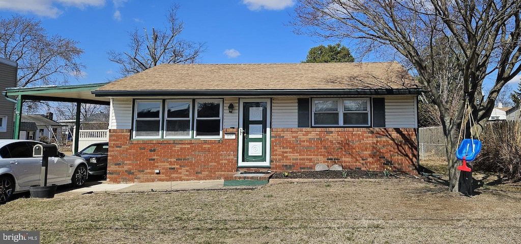 view of front of house featuring fence, a front yard, a shingled roof, an attached carport, and brick siding