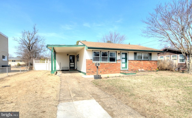 view of front facade featuring brick siding, fence, concrete driveway, a front yard, and a carport