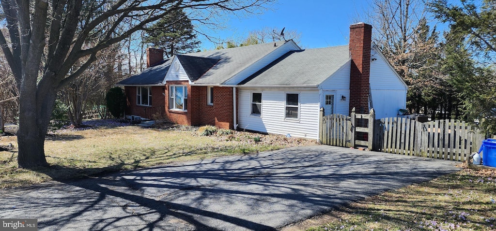 view of property exterior with aphalt driveway, brick siding, a chimney, and fence