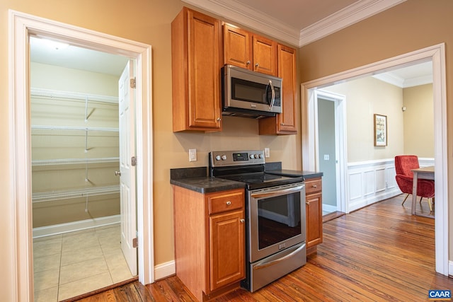 kitchen with wood finished floors, crown molding, appliances with stainless steel finishes, dark countertops, and brown cabinets