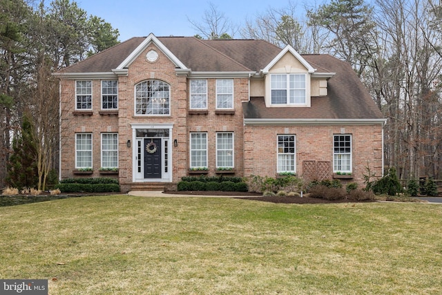 view of front of house with a front yard, brick siding, and a shingled roof