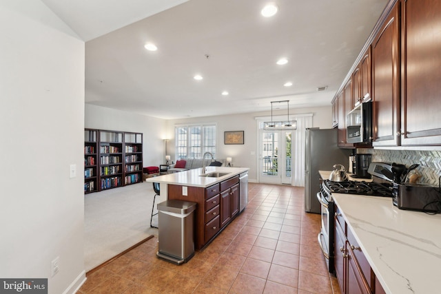 kitchen featuring a breakfast bar, a center island with sink, a sink, open floor plan, and stainless steel appliances