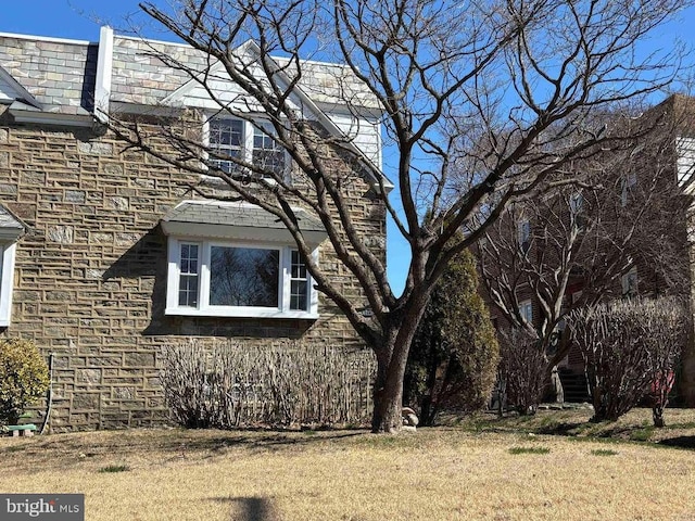 view of side of property with stone siding and a lawn