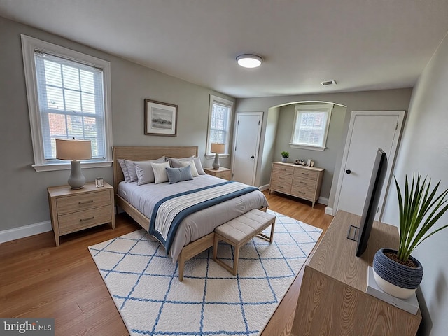 bedroom featuring visible vents, baseboards, arched walkways, and light wood-style flooring