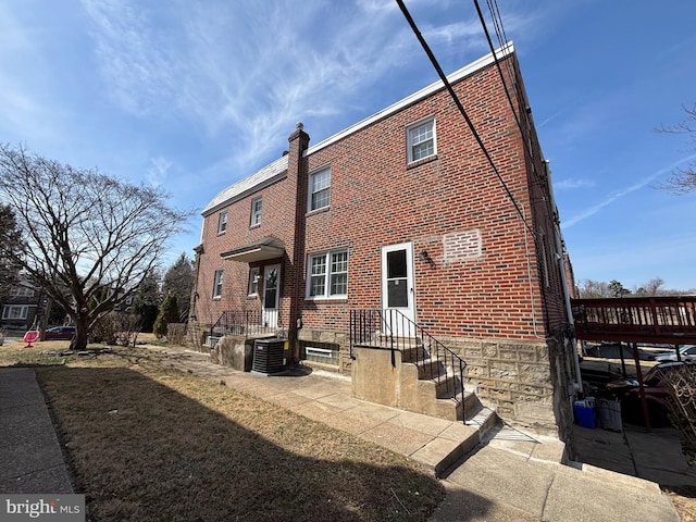 rear view of property with brick siding, central AC unit, and a chimney