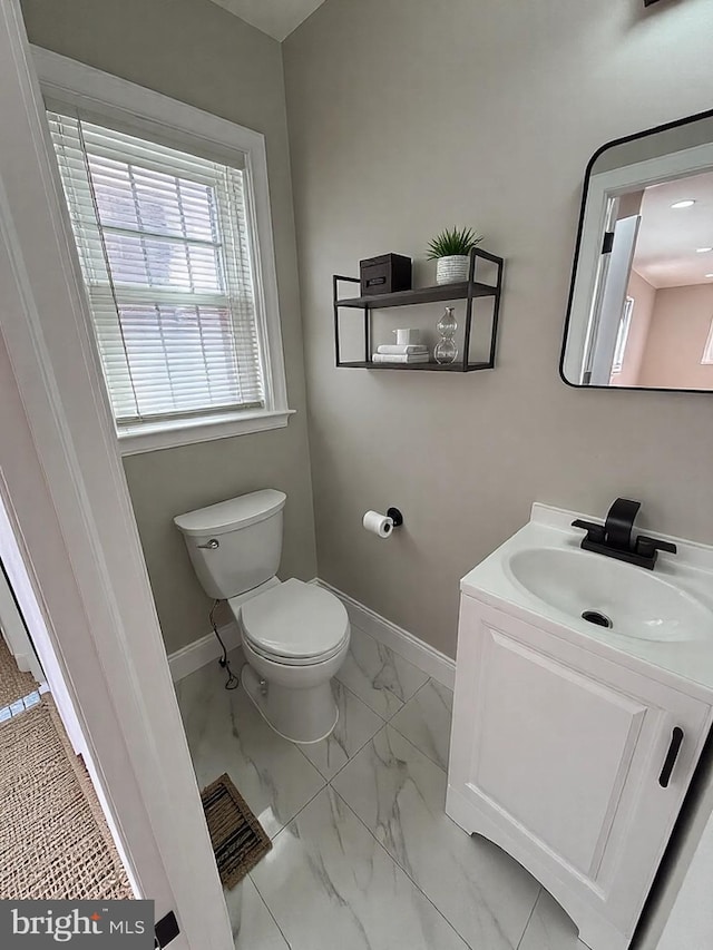 half bath featuring marble finish floor, toilet, vanity, and baseboards