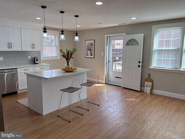 kitchen with tasteful backsplash, stainless steel dishwasher, wood finished floors, white cabinetry, and light countertops