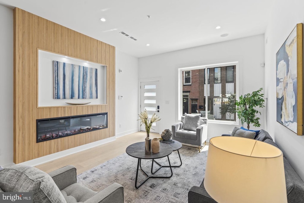 living area featuring a glass covered fireplace, recessed lighting, wood finished floors, and visible vents