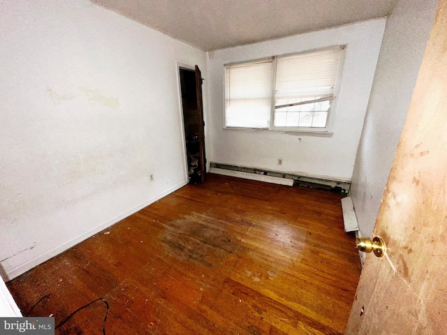 spare room featuring a baseboard radiator, wood-type flooring, and baseboards