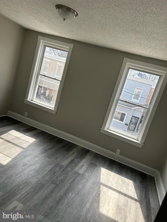 spare room featuring dark wood-style floors, a textured ceiling, and baseboards