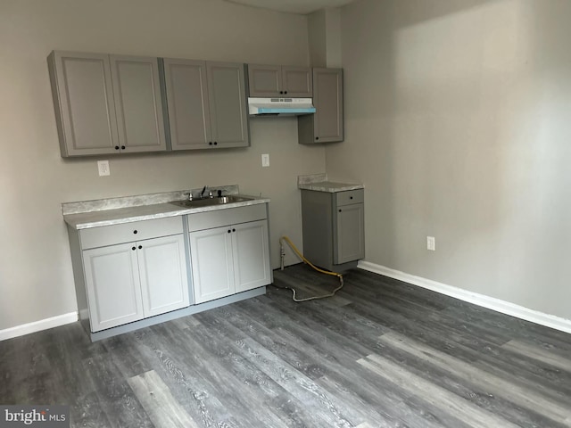 kitchen featuring baseboards, gray cabinets, under cabinet range hood, and a sink