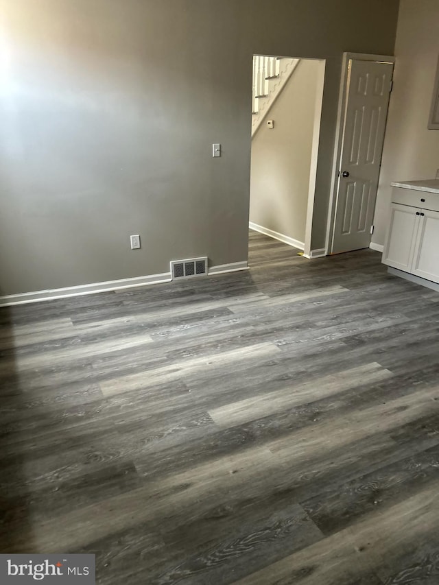 empty room with dark wood finished floors, visible vents, stairway, and baseboards