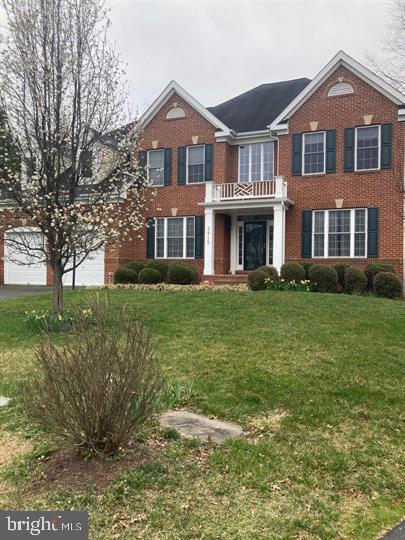 georgian-style home featuring brick siding, driveway, an attached garage, and a front lawn