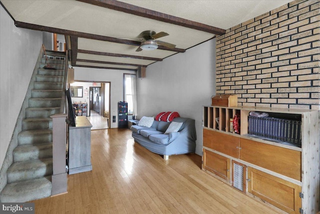 living room with a ceiling fan, beam ceiling, light wood-style flooring, stairs, and a textured ceiling