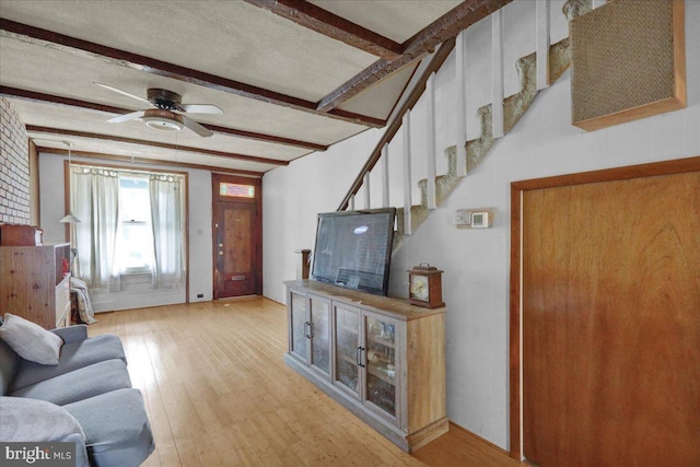 living room featuring stairway, beamed ceiling, ceiling fan, and wood finished floors