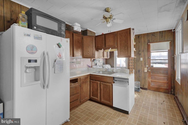 kitchen featuring a sink, white refrigerator with ice dispenser, wood walls, and black microwave