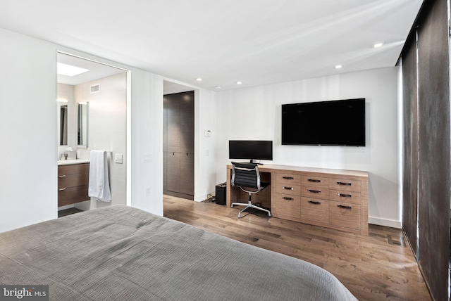 bedroom with built in study area, recessed lighting, wood finished floors, and connected bathroom