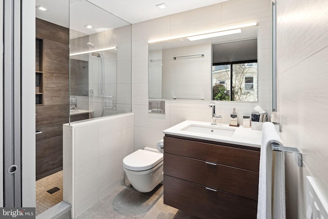 bathroom with tile patterned floors, toilet, a tile shower, tile walls, and vanity