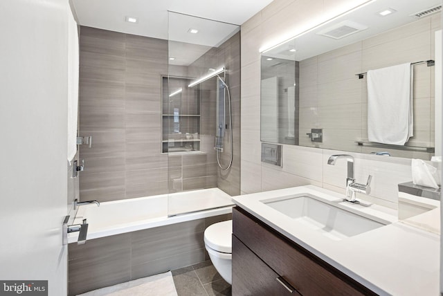 full bath with visible vents, toilet, vanity, tiled shower / bath combo, and tile walls