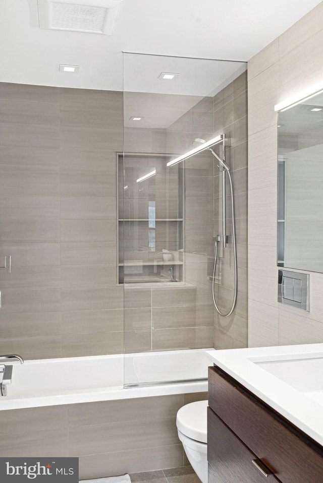 bathroom featuring vanity, tile walls, toilet, and tiled shower / bath