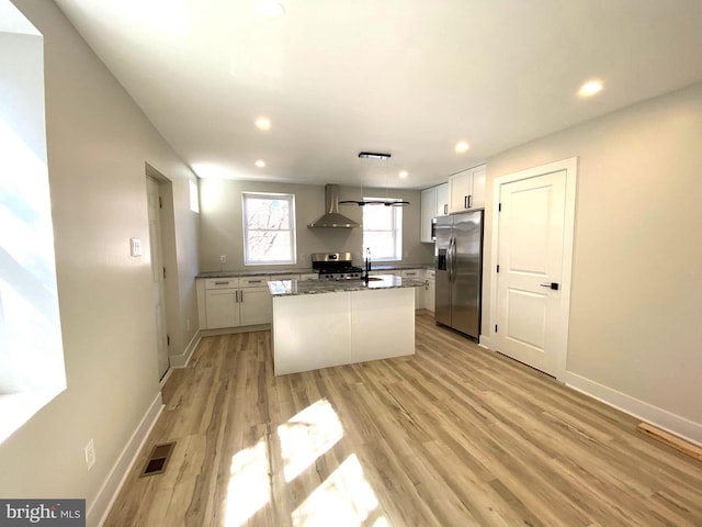 kitchen featuring wall chimney range hood, white cabinets, light wood finished floors, and stainless steel appliances