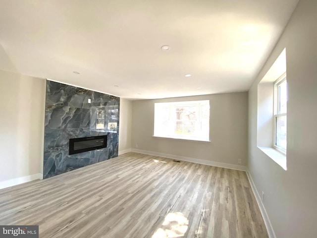 unfurnished living room featuring visible vents, wood finished floors, baseboards, and a high end fireplace